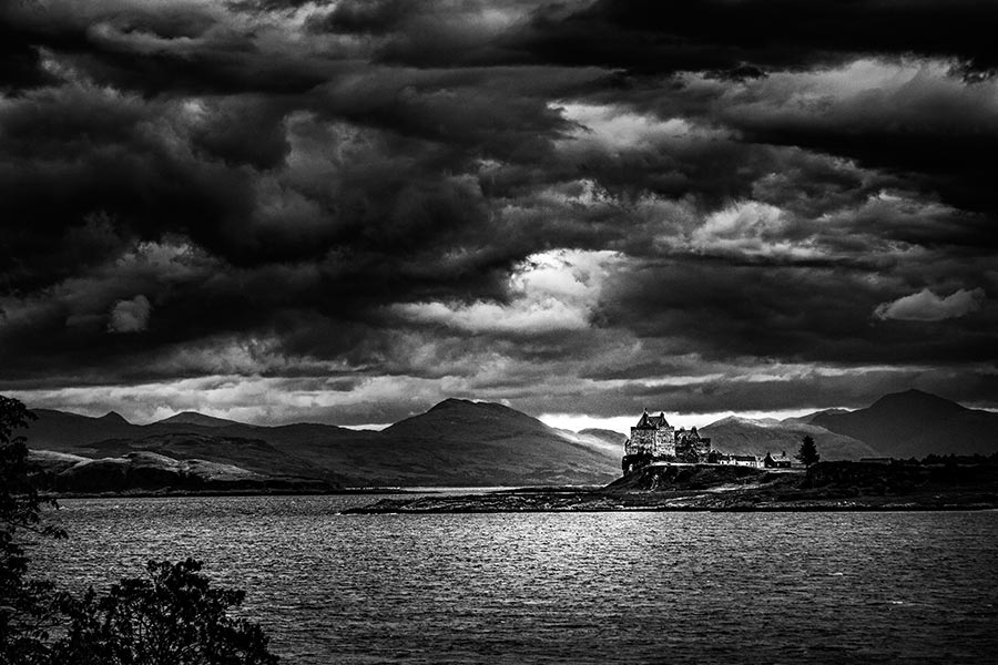 moody black and white photograph of dark skies over duart castle on the isle of mull in scotland