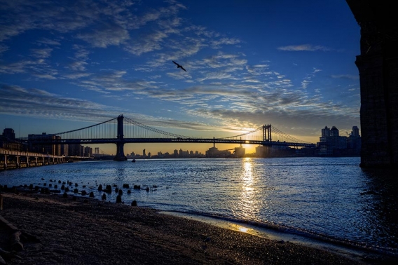 sunset behind manhattan bridge in new york city taken from under brooklyn bridge