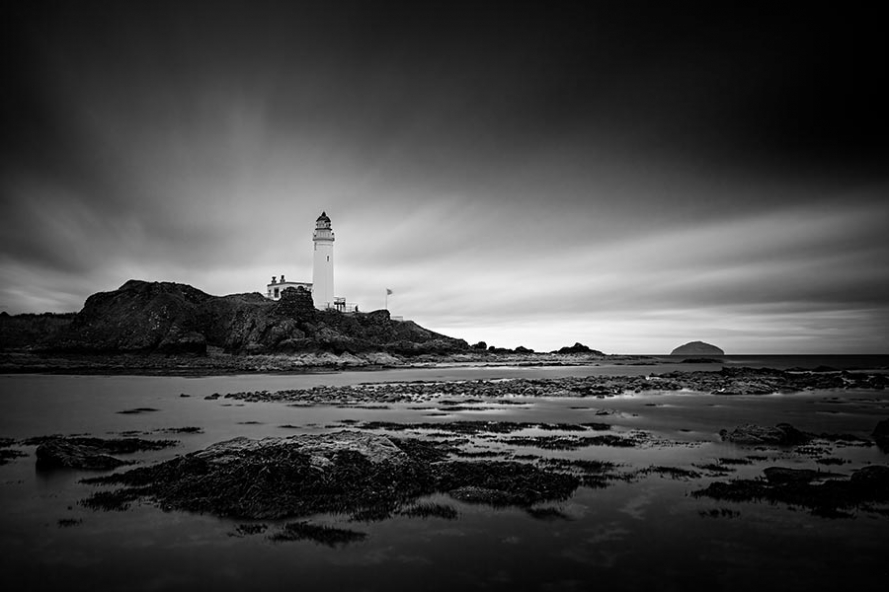 black and white photo of turnberry lighthouse in scotland from rocks at low tide